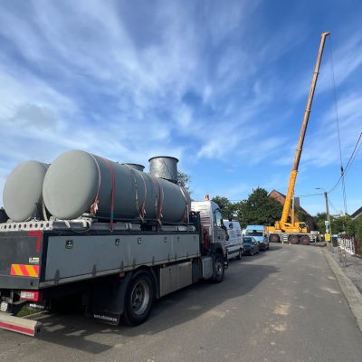 Camion transportant des citernes de propane dans une rue résidentielle, avec une grue déployée à l’arrière-plan pour préparer leur levage sur le chantier.
